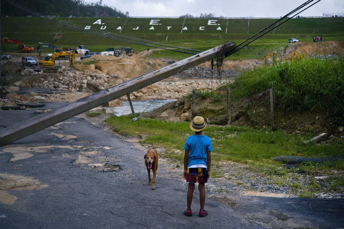A boy accompanied by his dog watches the repairs of Guajataca Dam, which cracked during the passage of Hurricane Maria, in Quebradillas, Puerto Rico, Tuesday, Oct. 17, 2017. The dam was built around 1928, and holds back a man-made lake. (AP Photo/Ramon Espinosa)